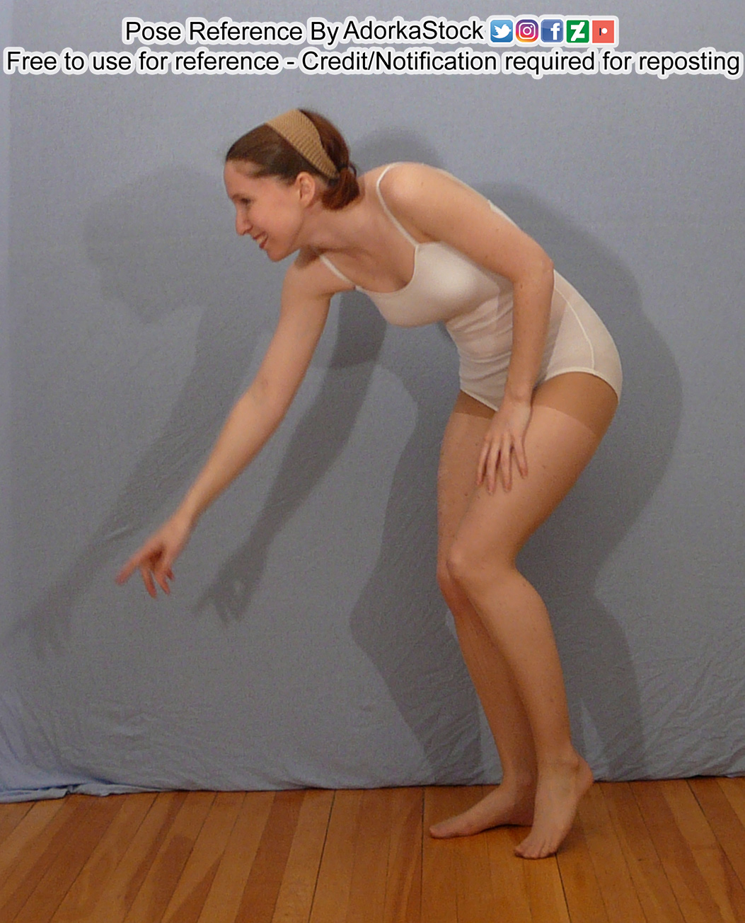 A white woman bent over slightly, a finger pointing towards the ground, smiling, a hand on her thigh.