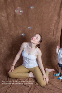 A white woman sitting down, legs loosely folded beneath her, looking up at four bubbles above her.