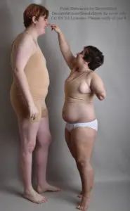 A very tall white model with a very short white model reaching up to poke them on the nose