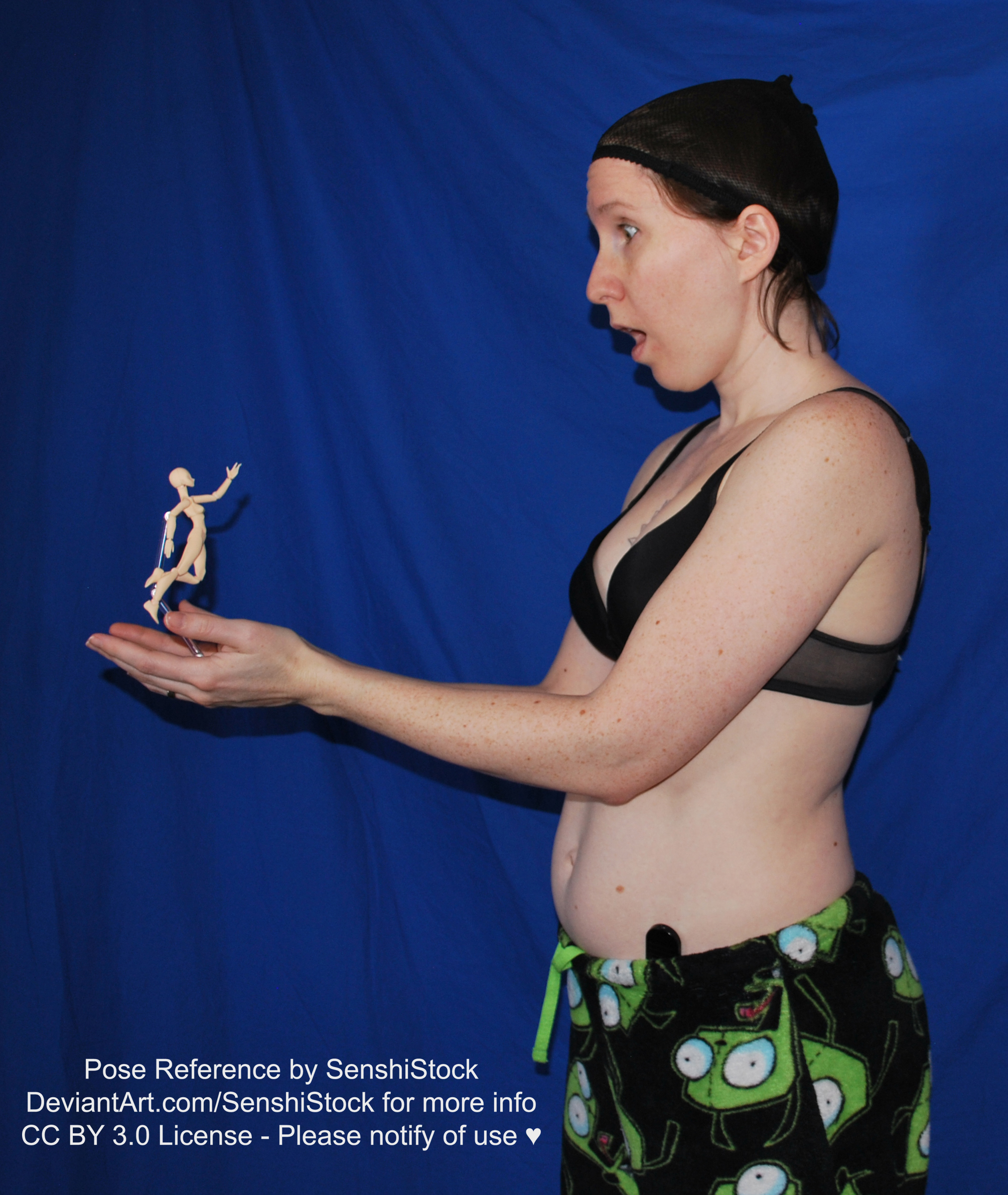 A white woman wearing a black bra and Gir pajama bottoms from the side, holding out her hands to the left, and cupping a small jumping figure in hand. She looks surprised.