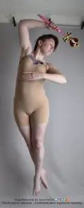 A white woman, jumping in the air and appearing to levitate, holding a Sailor Moon style wand over her head and looking off to the side.
