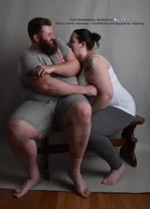 two fat models sit on a bench together the shorter female model is trying to bite the taller male model who is trying to push her away