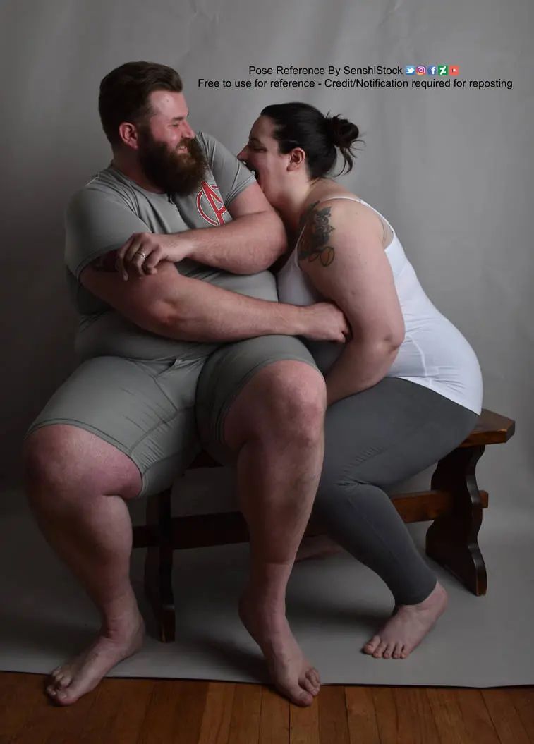 two fat models sit on a bench together the shorter female model is trying to bite the taller male model who is trying to push her away