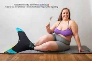 fat while female model sitting on the floor wearing a mermaid fin and holding a fork