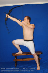 A white man in skin tight shorts, one leg up on a bench, aiming with a bow up towards the upper left.