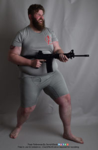 A fat white model wearing skin tight clothing is standing, legs apart, while holding a gun, pointed to the right, with proper trigger finger, and having an excited expression as if he's going to fire and have a great time doing it.