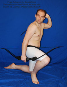 A white man, crouched down on one knee, holding a bow in his right hand, reaching back to his quiver with his left.