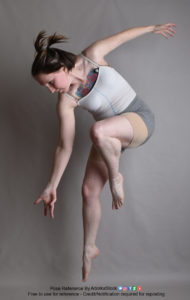 Thin white woman wearing white sports bra and form-fitting grey shorts, caught in mid-air leap downward, one leg raised at her chest, the other almost straight out. One arm is flung backward, the other is reaching downward, palm up. She's looking down.
