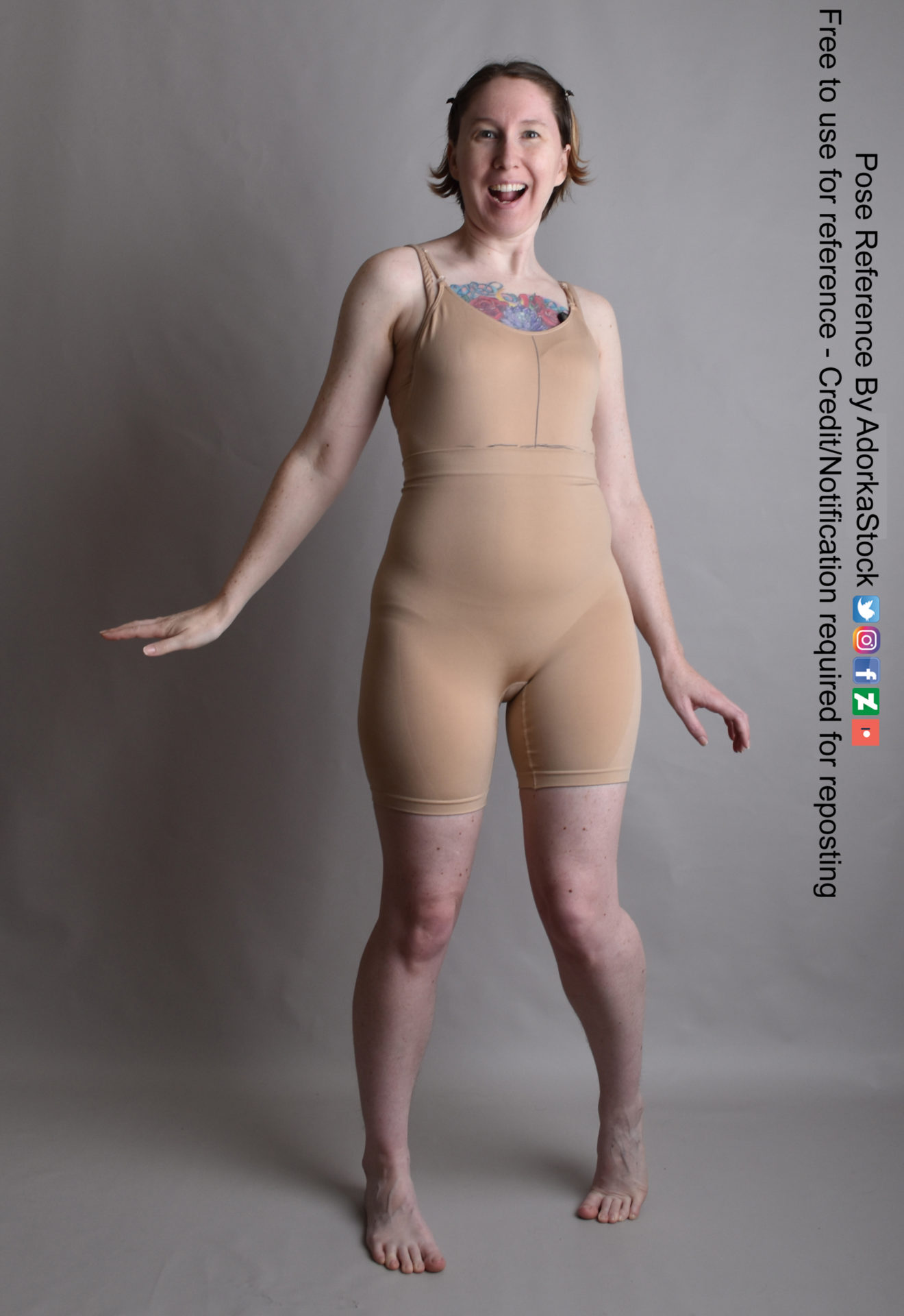 Thin white woman wearing a form-fitting beige body suit, standing with her toes slightly pointed inward, arms down at her side, with a massive grin on her face.