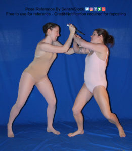 Two thin white women wearing leotards are standing, engaged in a fight with each other, one holding a knife to the other.