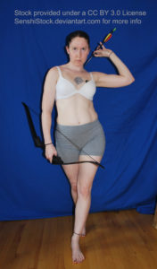 White woman walking forward towards the viewer, one arm over her right shoulder gripping an arrow from her back, her left hand holding a bow down by her thigh. Her facial expression looks determined. She is wearing a white bra and grey bike shorts.