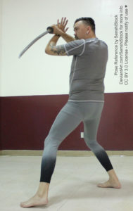 A white man wearing a grey gym suit standing, back to the camera, making a stabbing motion with a katana.