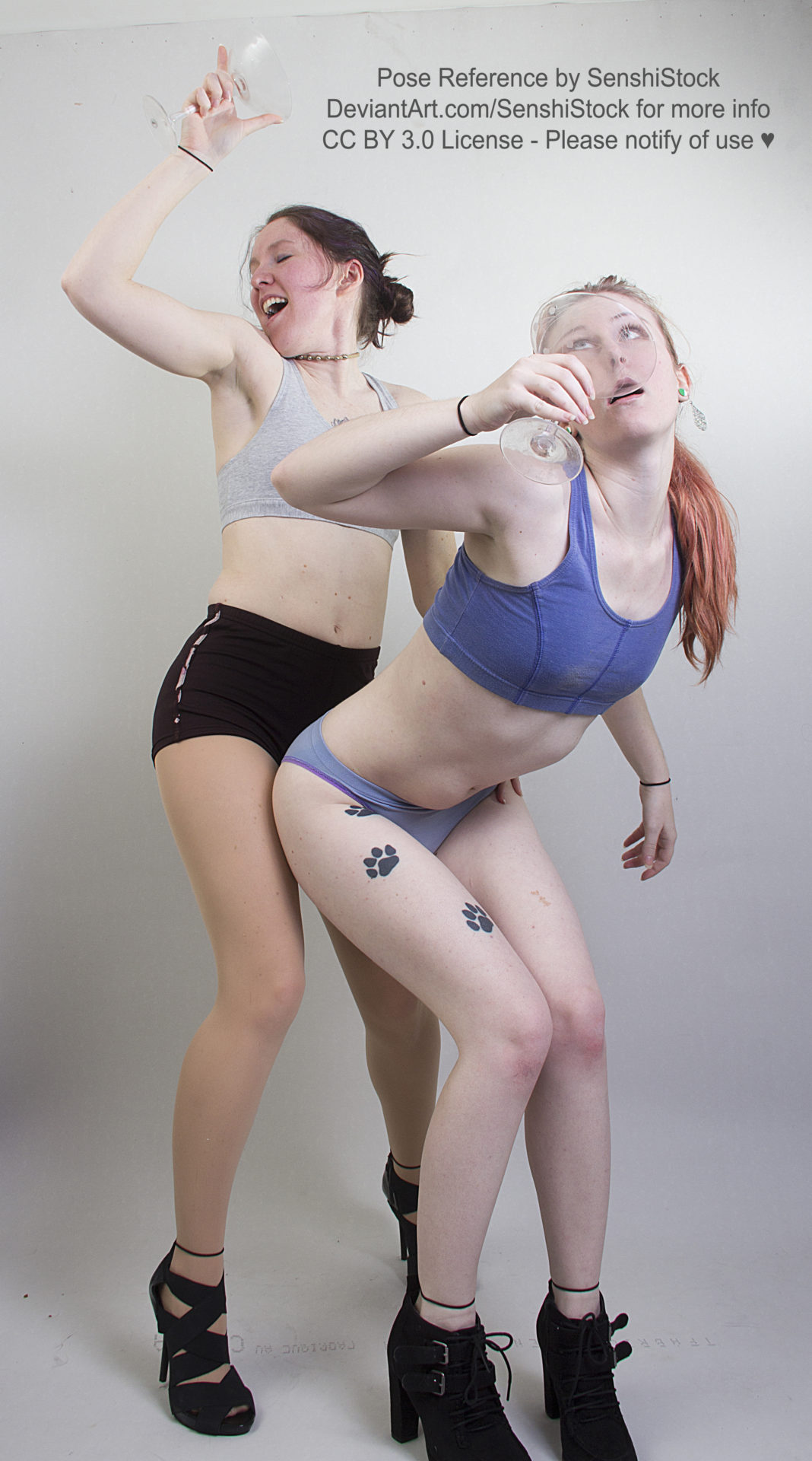 Two thin, white, female models wearing sports bras and short shorts with black high heels, are drunk dancing, margarita glasses in hand. One is leaned over guzzling down her drink, the other is grinding up behind her.