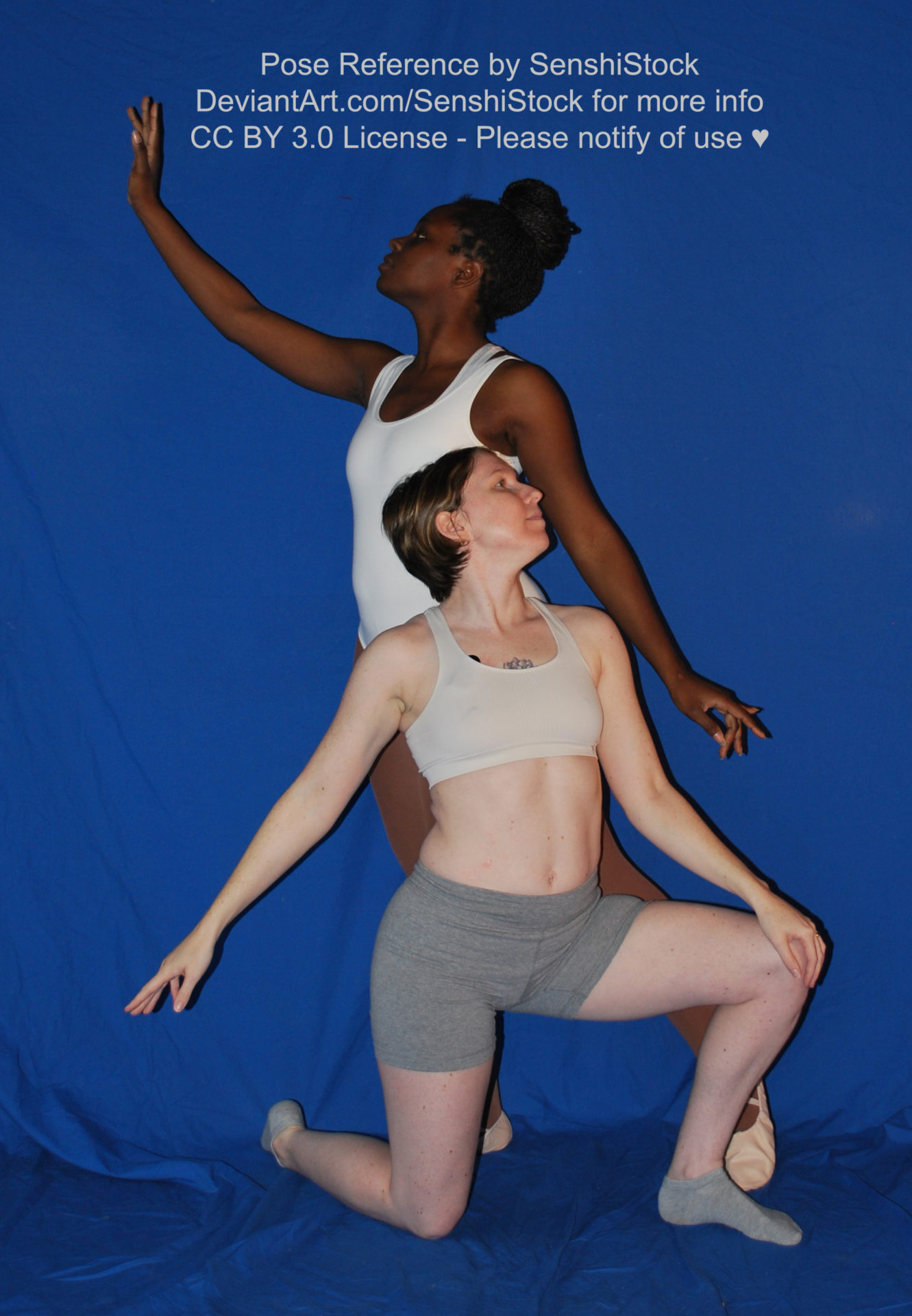 Two women, one white and the other black, wearing skin tight clothing, one standing, the other down on one knee as they face away from each other and hold out their arms elegantly.