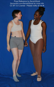 Two women, one white and the other black, wearing skin tight clothing, standing together and holding hands.