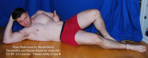 A muscular white man wearing a pair of red boxers is laying on his side on the floor, one knee bent and up, the other leg straight out, one arm holding up his head, the other giving you a thumbs up as he's giving an approving smile.