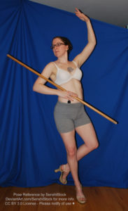 A white woman wearing heels dancing with a staff in the crook of her elbow.