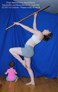 A white woman lifting a staff up into the air, one knee in the air, one foot on the ground.