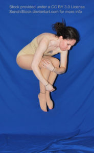 White woman jumping in the air, arms curled around her knees which are up by her chest.