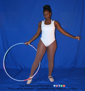 Thin black woman wearing a white one piece skin-tight bodysuit and pointe shoes is standing facing the camera, legs and arms apart, with one hand holding a hula hoop, with one of her feet wrapped around it.