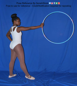Thin black woman wearing a white one piece skin-tight bodysuit and pointe shoes is standing 3/4, with her back mostly to the camera. Legs are apart and her arm is out and holding up a hula hoop.