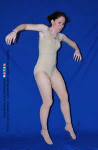A white woman on a blue background coming down from a leap, both arms extended on either side of her.