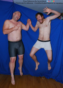 Two white men with boxers jumping in the air with big grins on their faces, and holding each other's hand. One pointing a finger gun at the other.