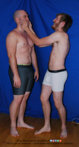 Two white men with boxers standing, one with both hands pinching the cheeks of the other.