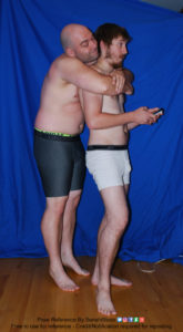 Two white men with boxers with one on his phone, surprised, as the other hugs him from behind.