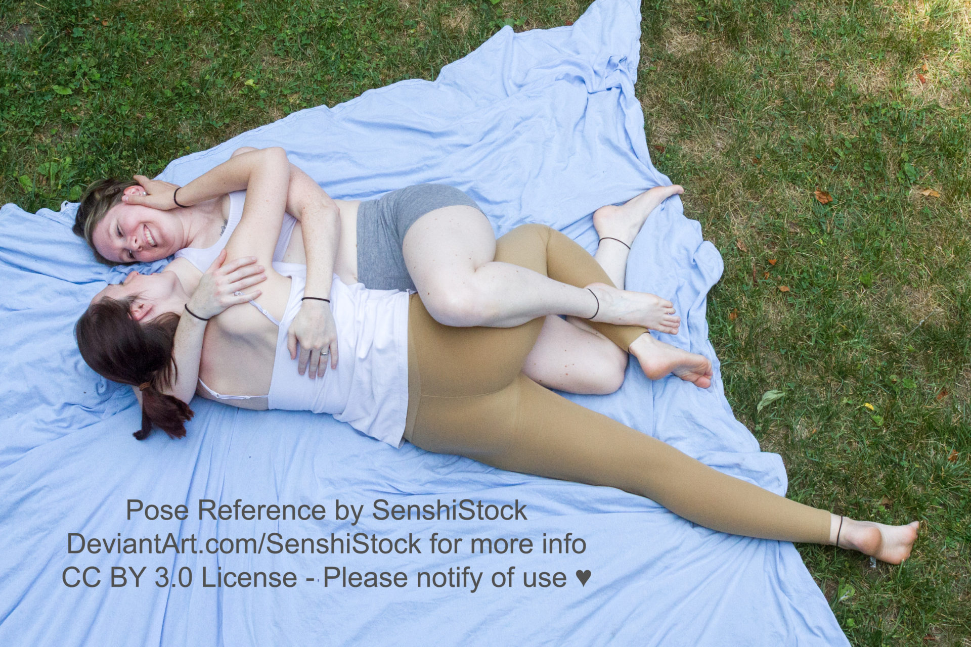 Two thin white women seen from a bird's eye view, 3/4, laying down cuddling with each other, legs and arms intertwined as they're looking at each other and smiling.