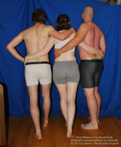 A group of three white people, two men and one woman, are standing in a line, seen from the back, with the woman in the middle, all of them wrapping their arms around each other.