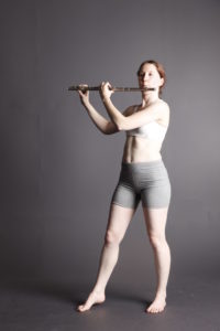 White woman on a grey background playing a flute.