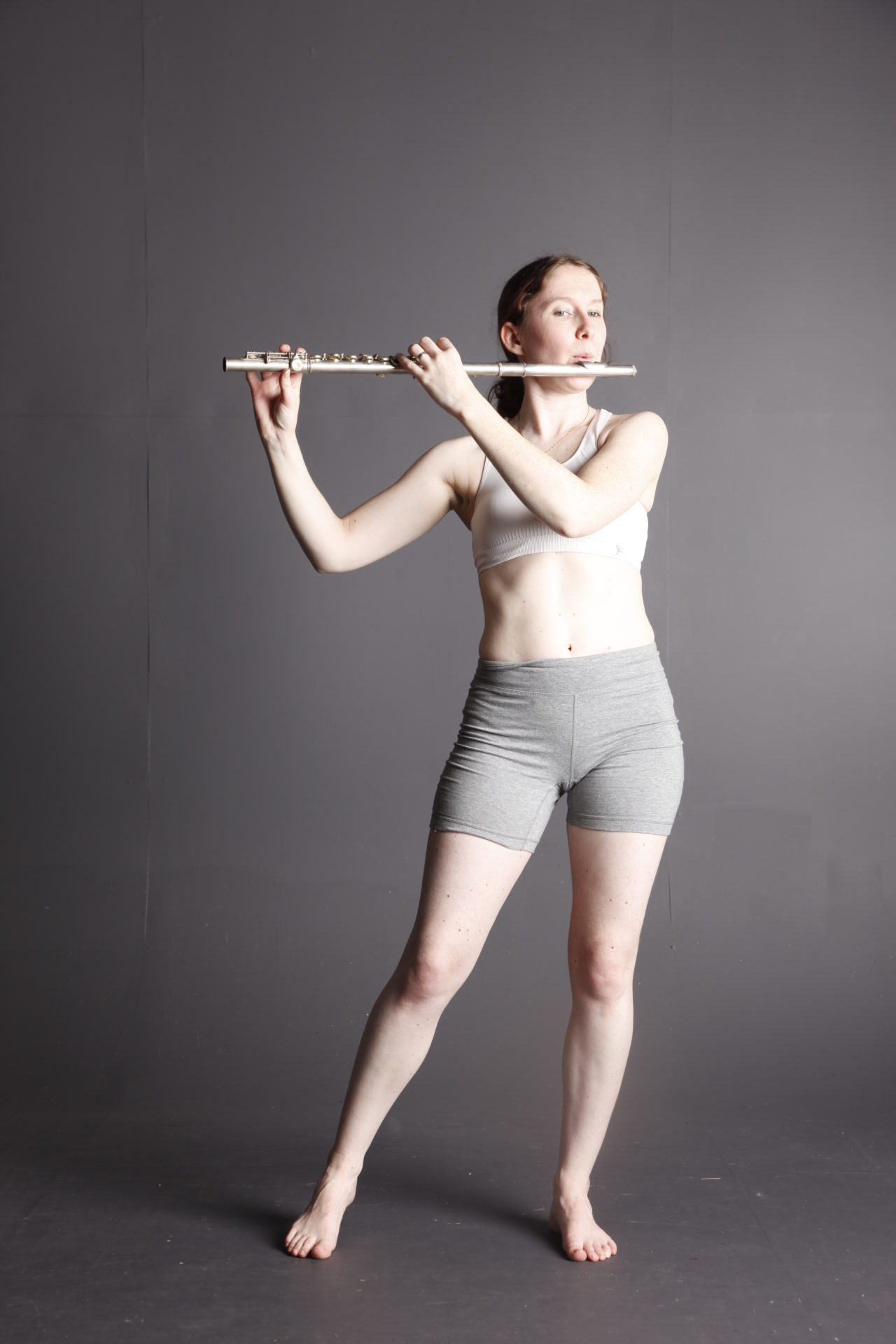 White woman on a grey background playing a flute.