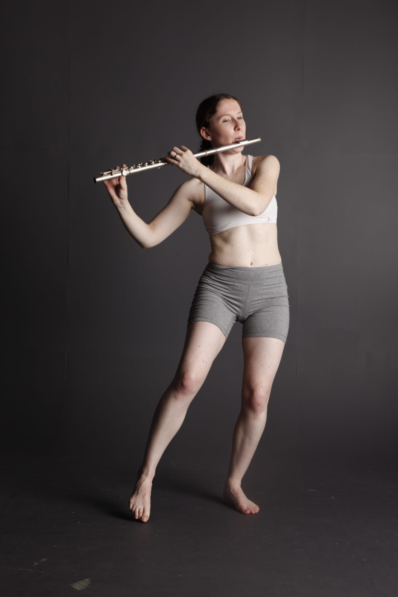 White woman on a grey background playing a flute.