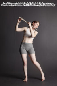 White woman on a grey background playing a flute.