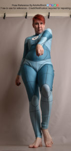 A person wearing an aqua colored body suit with grid lines on it, taken from a low angle, pointing up. The person is facing the camera and pointing their left finger accusingly at the camera.
