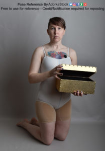 White woman on her knees in a white leotard holding a partially opened golden box in one hand, opening it with the other.