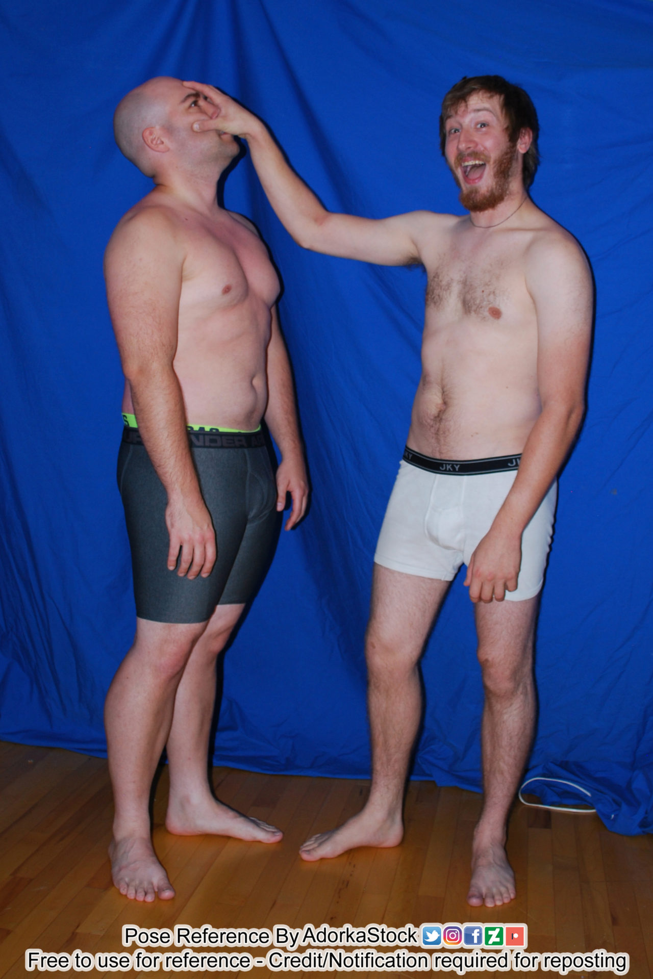 Two white male models one standing with arms limp by his side, face turned up while the other is grabbing the first's face with his hand and looking at the camera and smiling ridiculously.