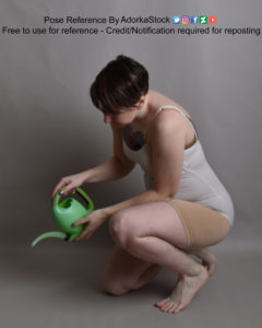 White woman crouched on the ground holding a small green watering can and watering something invisible.