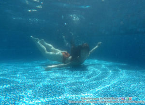 A underwater shot of a thin, fit woman, swimming with her chest against the bottom of the pool, legs up behind her and floating, with her arms outstretched to her side, as if she's flying.
