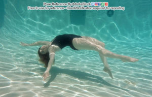 A white woman in a black one piece bathing suit, arching backwards, one leg extended gracefully, along with one arm.