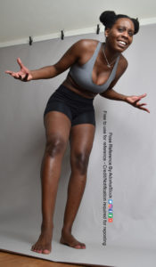 pose reference of a black, fit, female model with arms out to the side as if confused - the photo is shot from a low angle and the model is leaning over the camera slightly