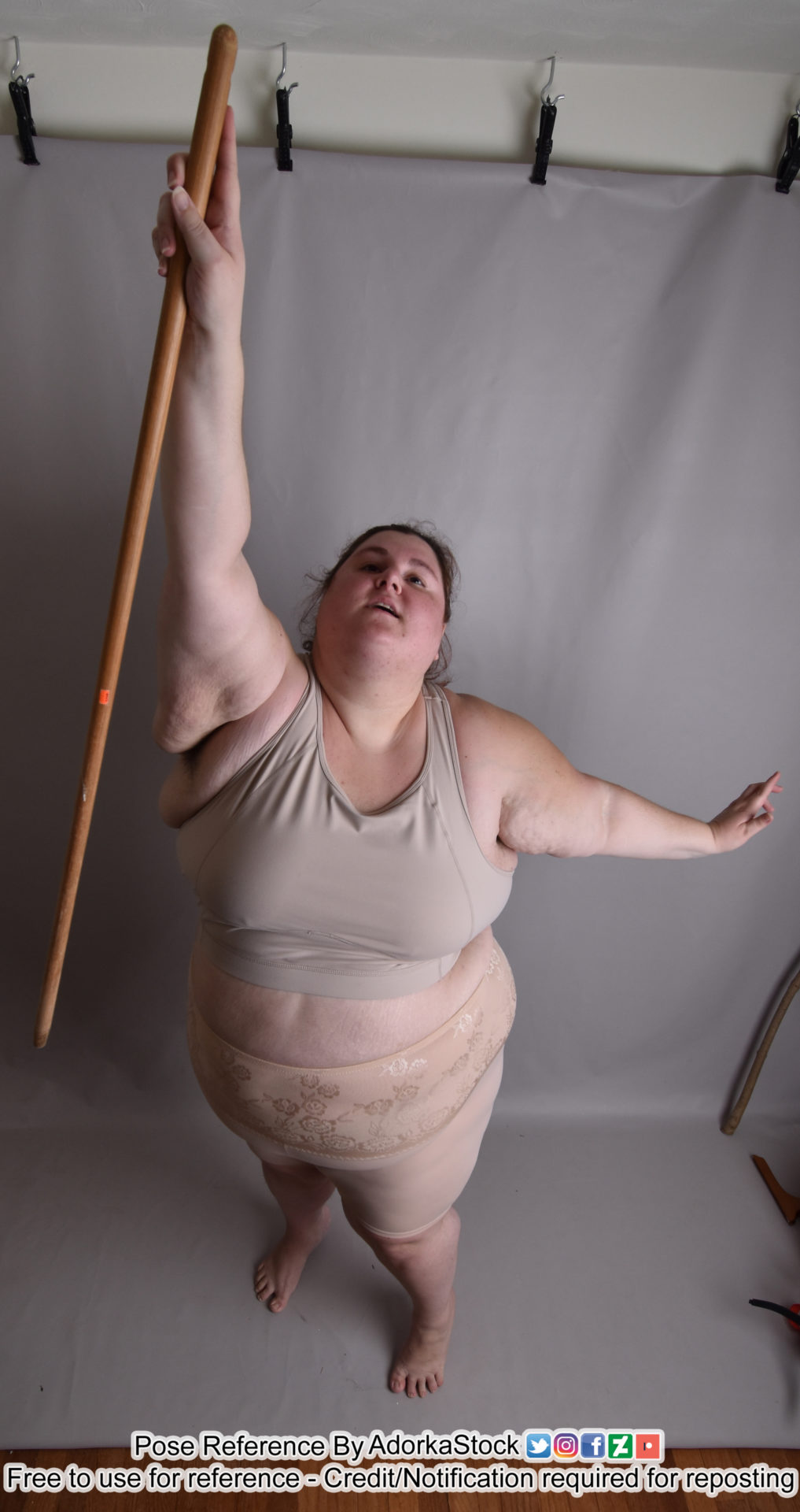 fat female white pose reference model from a high perspective, reaching up one hand with a staff