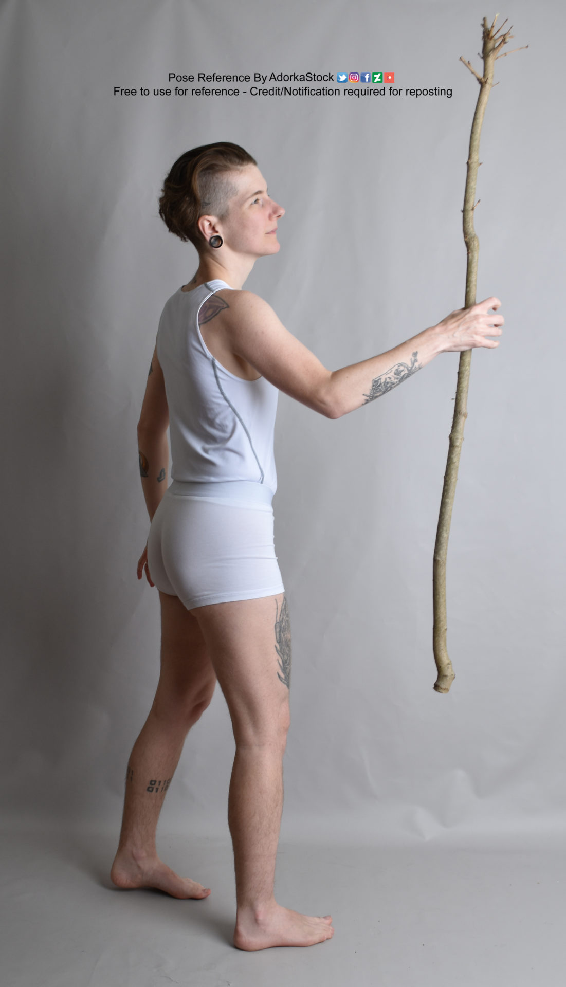 thin white nonbinary model facing 3/4 away holding a fancy looking magical stick up slightly with one hand while looking at it
