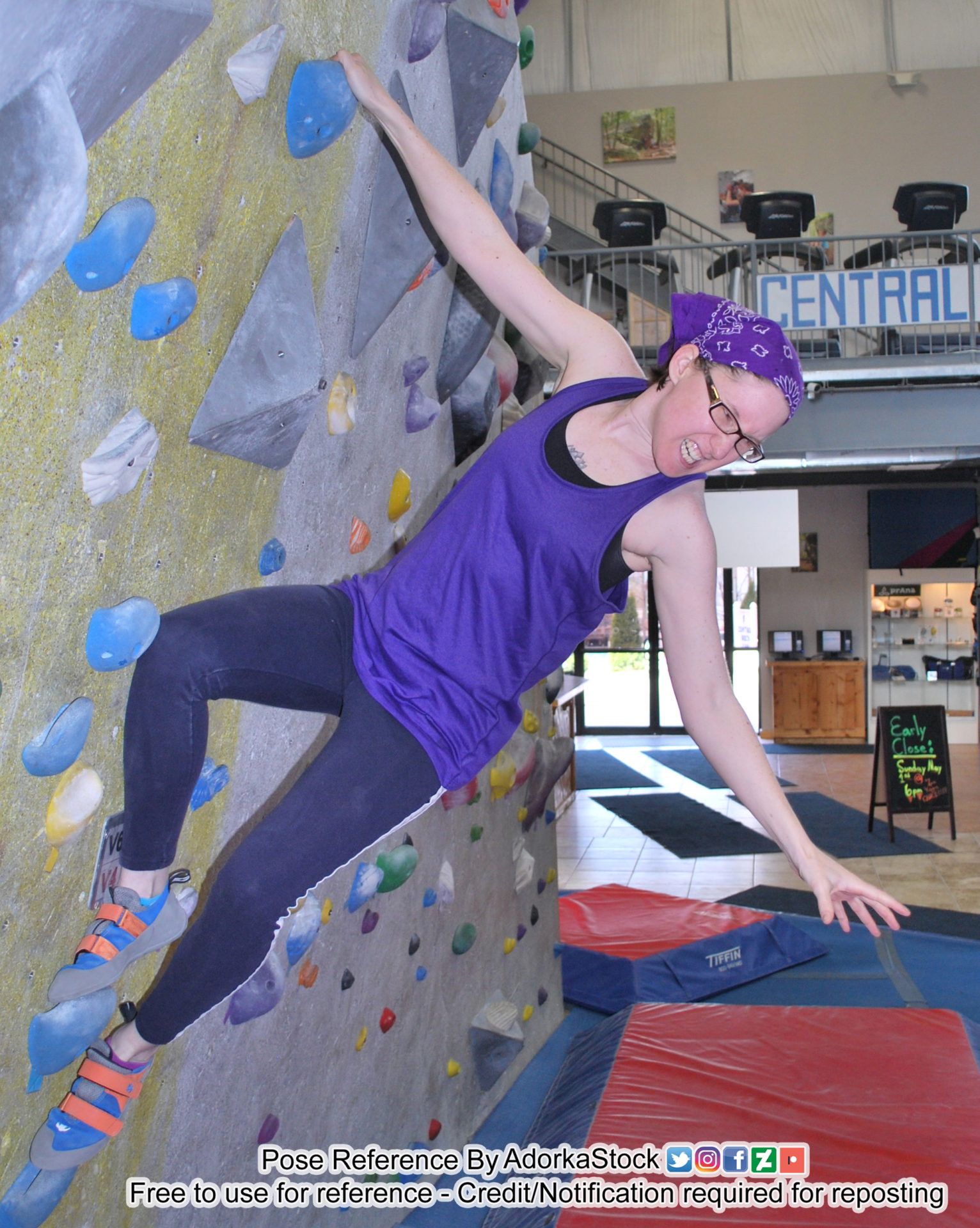 white, female, fit, pose reference model in sporty clothing hanging from a rock climbing wall reaching down and back dramatically