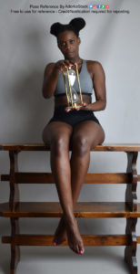Black, thin, female pose reference model sitting with legs dangling while holding an hourglass