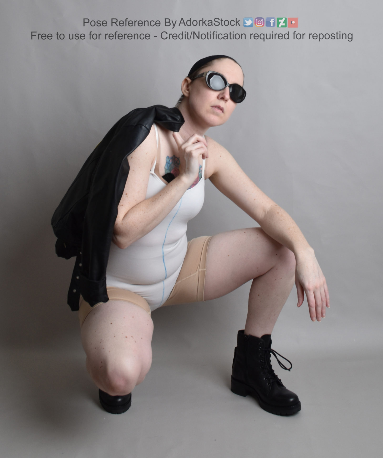 thin, white, female model squatting in boots with a leather jacket over one shoulder and sunglasses