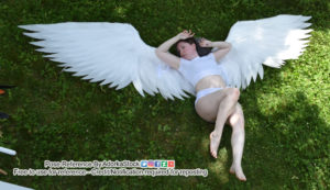 Thin, white, female model lying on the ground on top of outspread wings with one leg bent and her arms up by her face dramatically