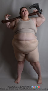 Heavy set woman in a grey sports bra and tan shapewear shorts, facing the camera and holding a Nordic style axe casually across her shoulders