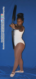 A woman in a white leotard and nude colored ballet flats facing the camera with her left foot forward, pointing a drawn bow with an arrow nocked on the string at the camera with a menacing look on her face